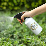 White 400ml aluminium spray bottle with black nozzle, held and spraying water in a garden