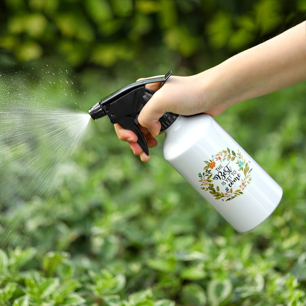 White 400ml aluminium spray bottle with black nozzle, held and spraying water in a garden