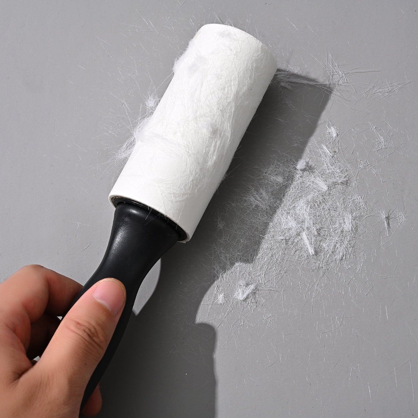 Used Lint Roller + Handle lifting pet hair from a surface, showcasing its strong adhesive power for effective fabric and home cleaning.