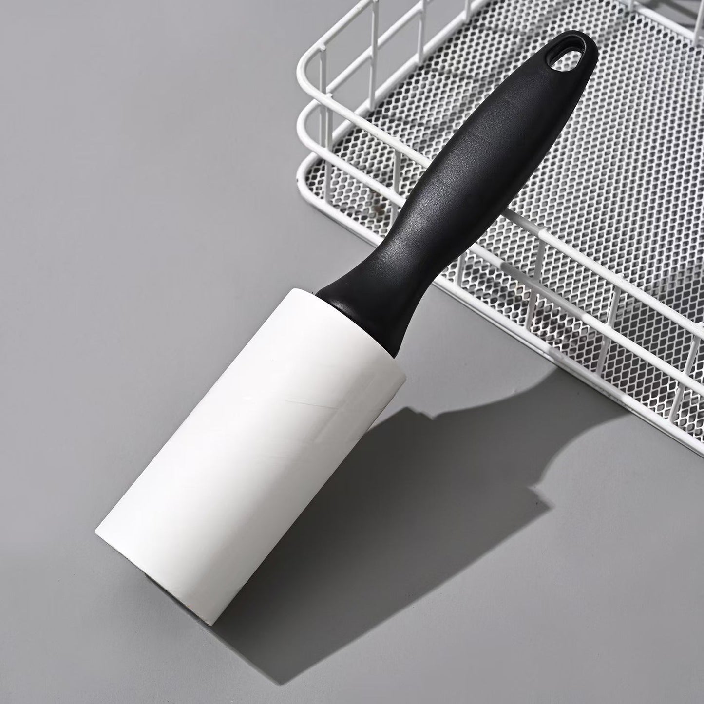 Reusable Lint Roller + Handle placed beside a mesh basket, perfect for laundry rooms or travel use in fabric care and lint removal.