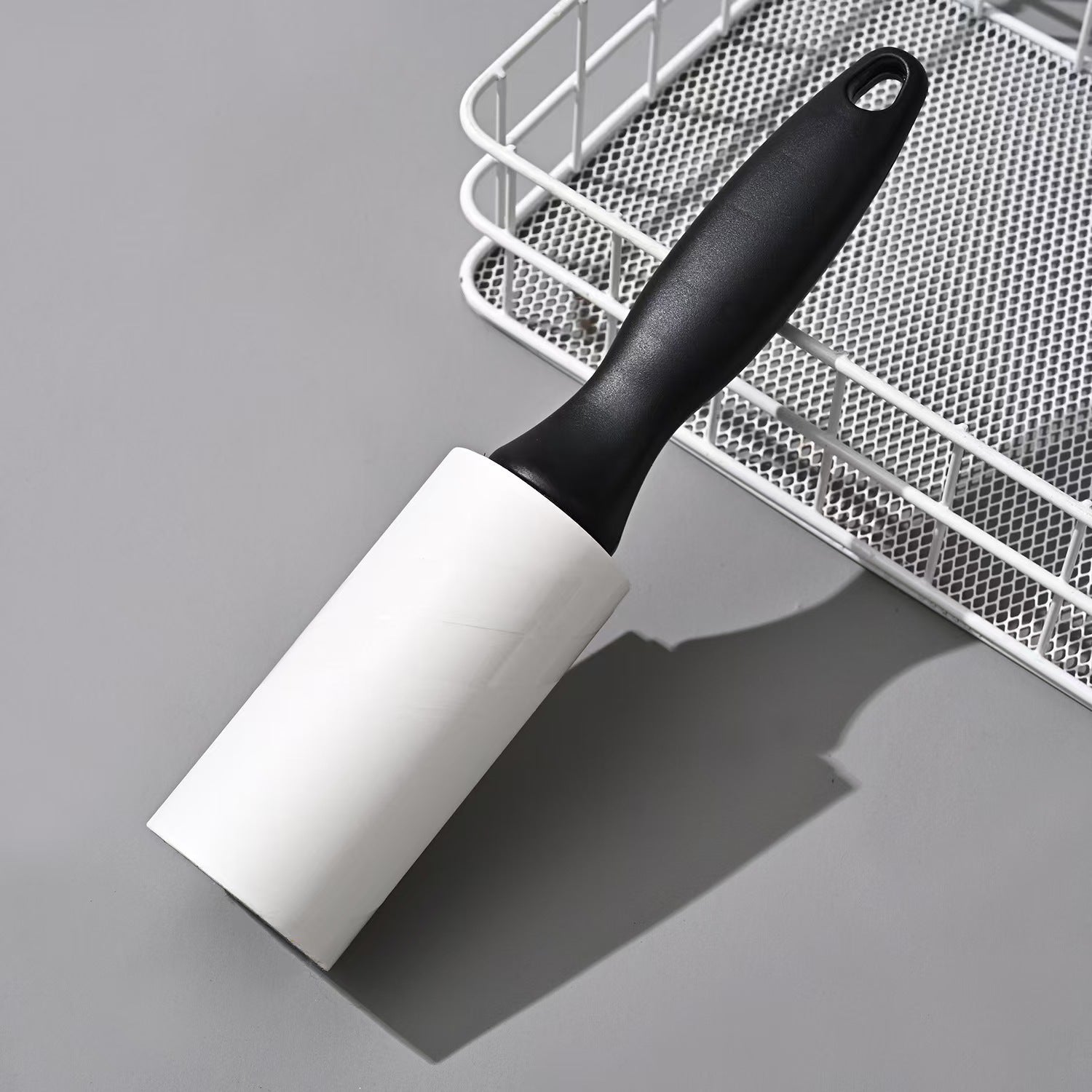 Reusable Lint Roller + Handle placed beside a mesh basket, perfect for laundry rooms or travel use in fabric care and lint removal.